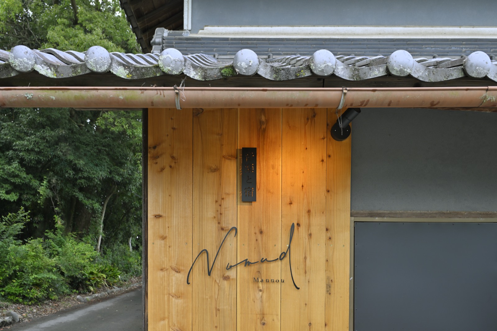 Nomad Mannouの看板。杉板に「Nomad Mannou」のサインと「音楽と宿」の木札が掛かっている
